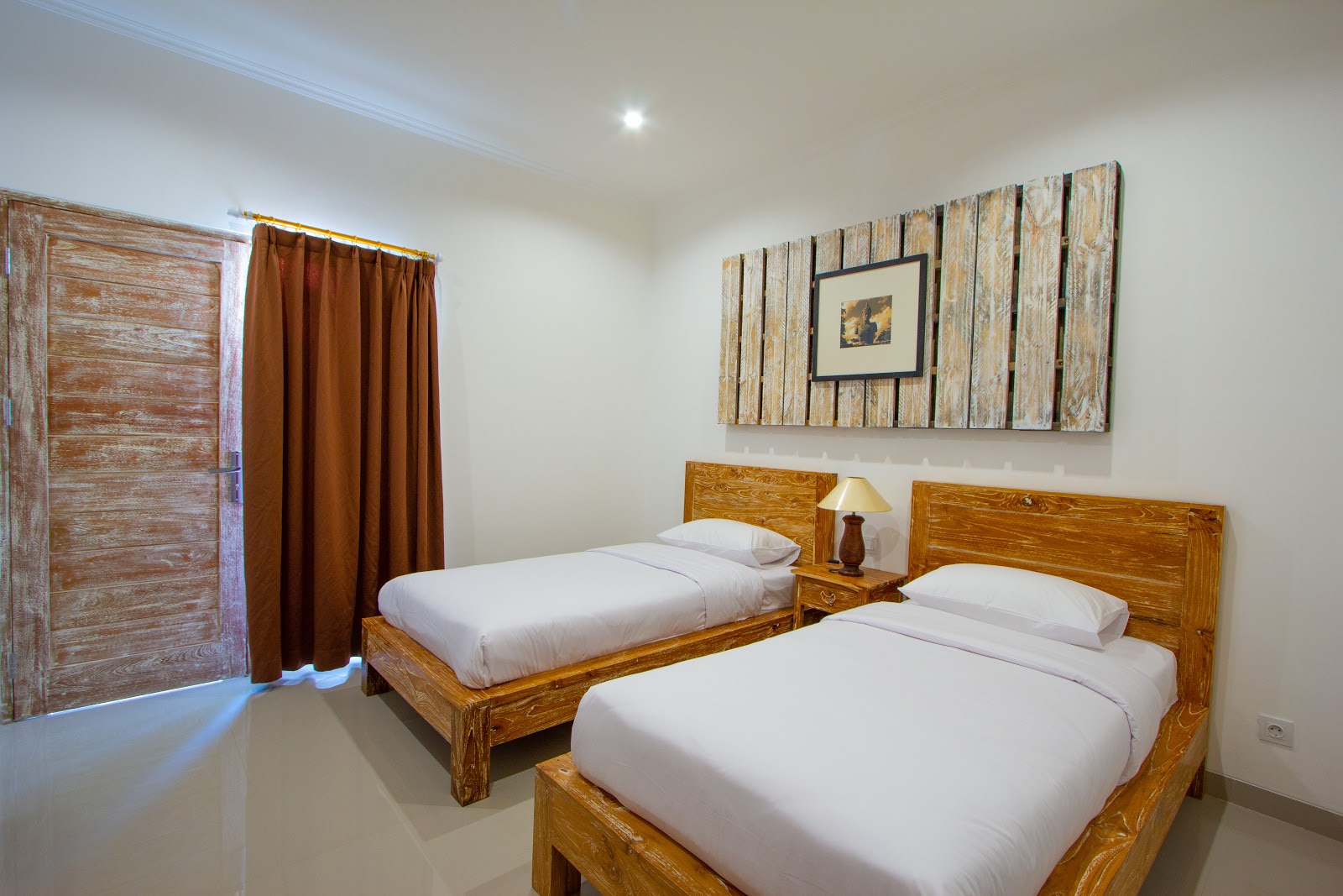 Twin bedroom with wooden beds, white linens, rustic wooden wall art, warm lighting, and traditional wooden door. Clean and well-organized guest room with modern amenities.